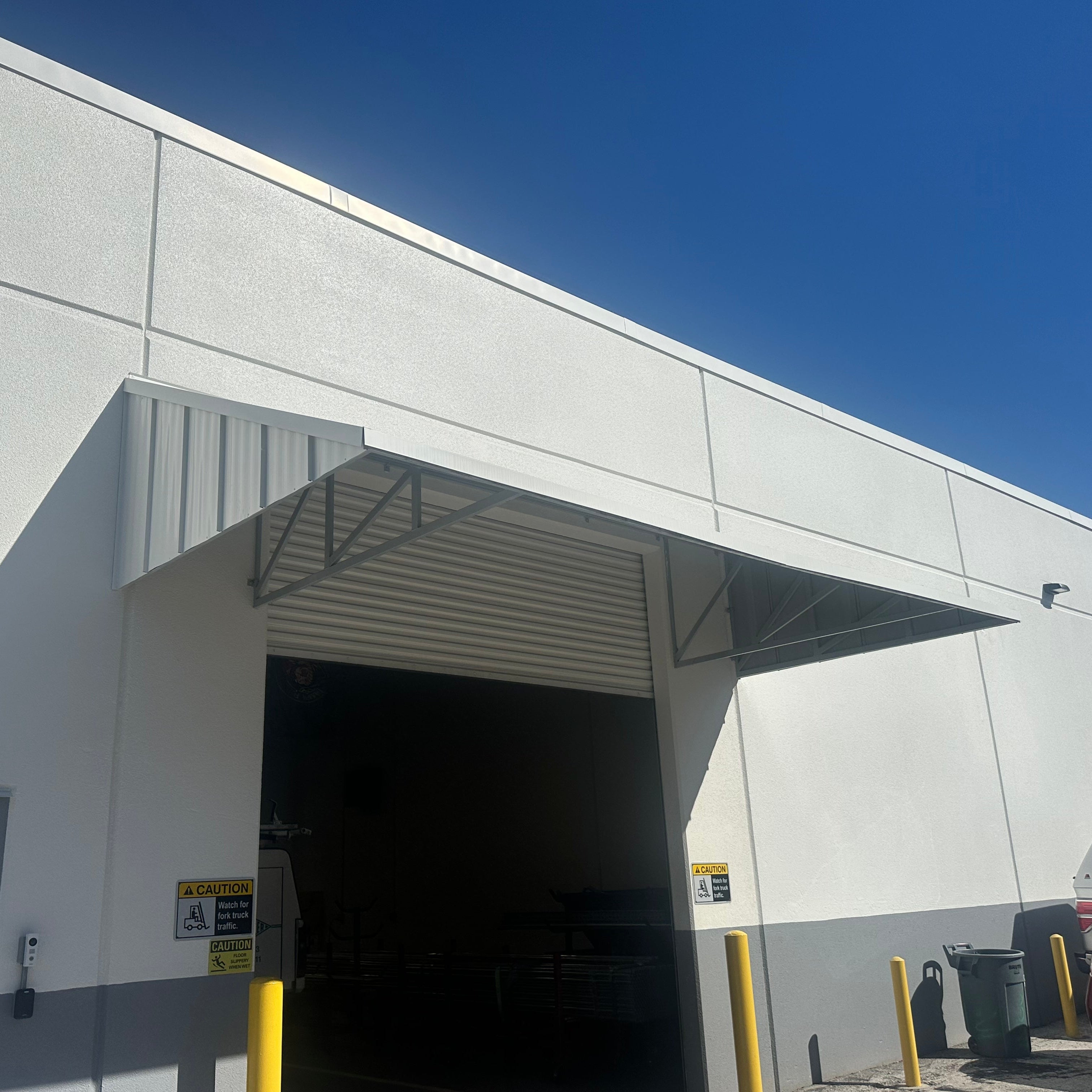 White industrial building with a large garage door, clear blue sky, and a red vehicle parked outside.