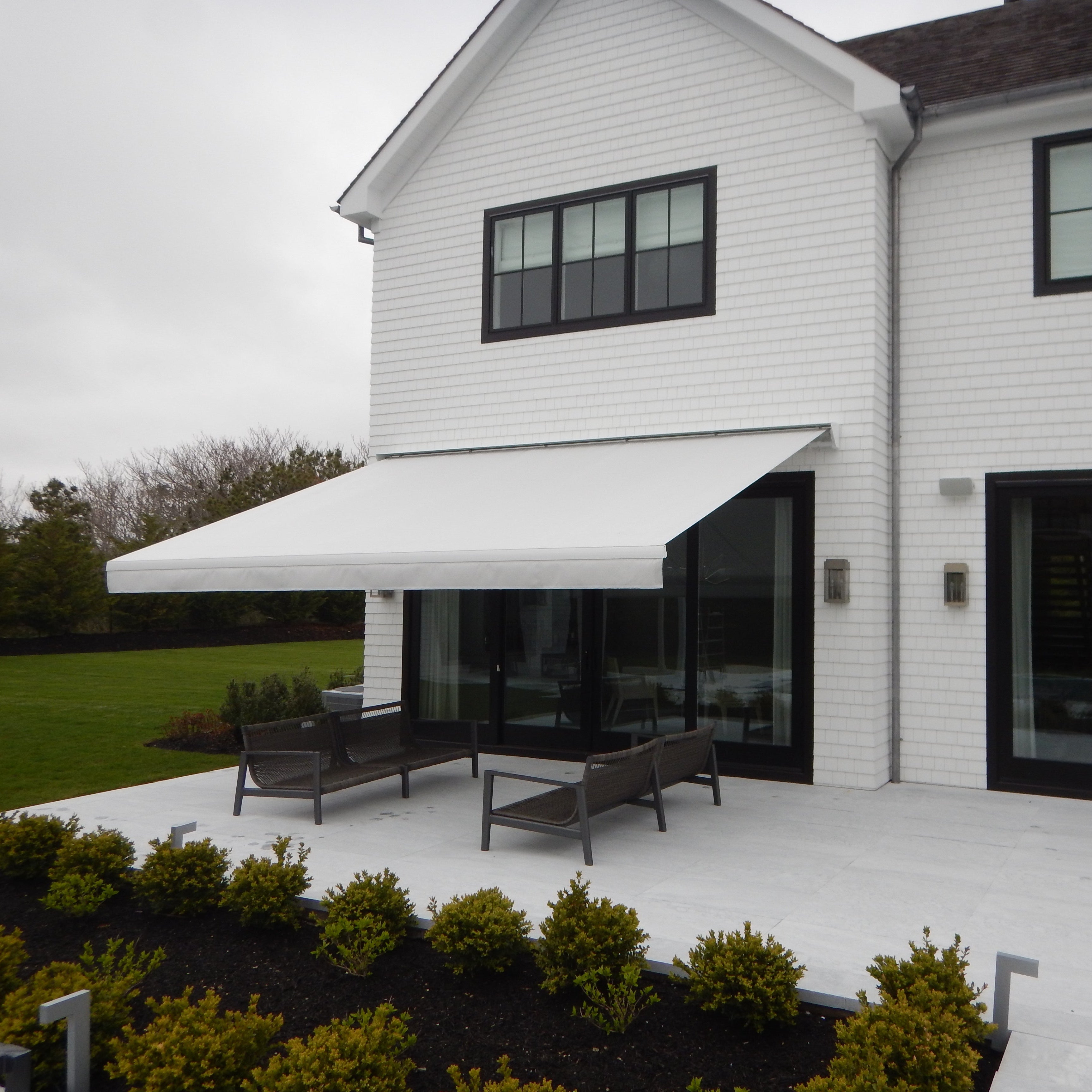 White house with a patio and outdoor furniture under an awning on a cloudy day.