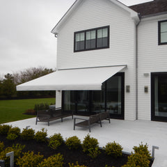 White house with a patio and outdoor furniture under an awning on a cloudy day.