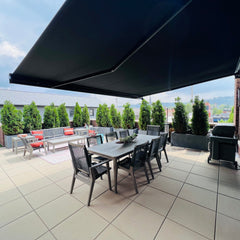Outdoor patio with dining table, chairs, and black retractable awning on a sunny day.